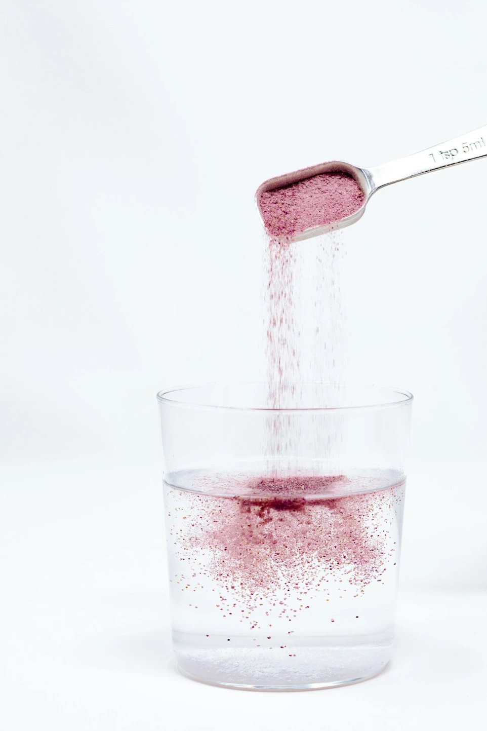 A spoon pouring red liquid into a glass